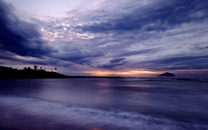 Ocean waves at sunset with dark clouds and island