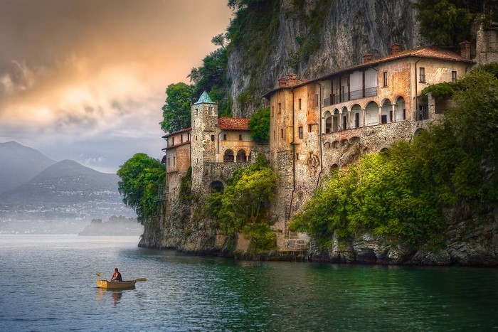 Monastery on a cliff overlooking a lake with a person in a boat