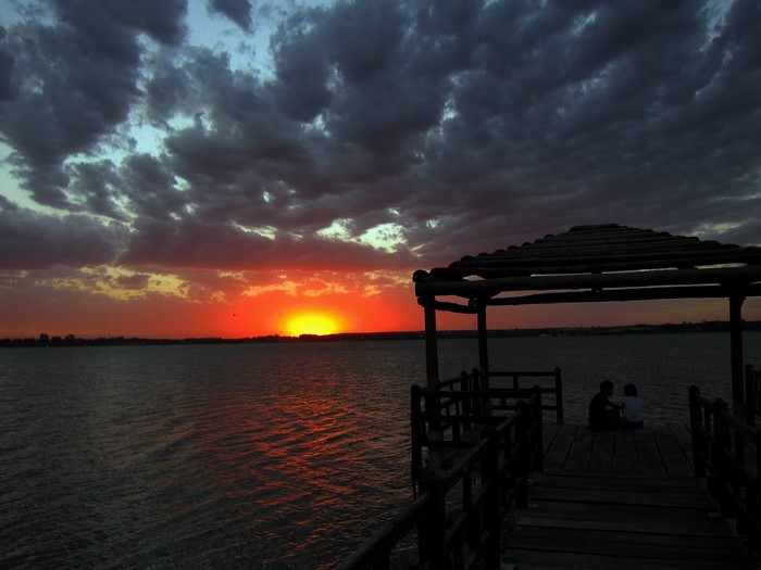 Two children on a pier watching a dramatic sunset over the ocean