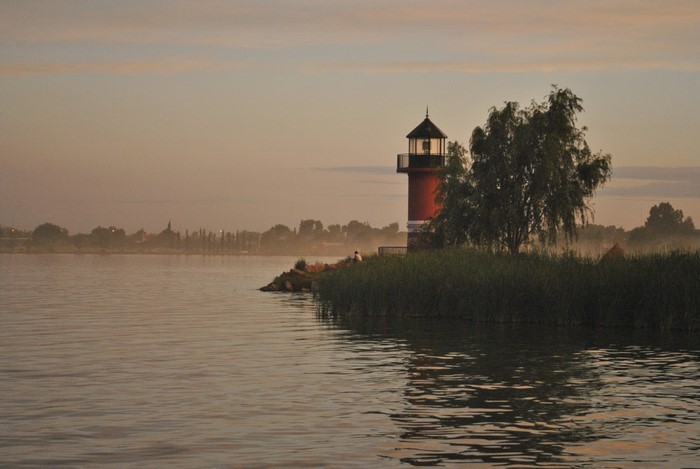 Red lighthouse on a misty shore at sunrise