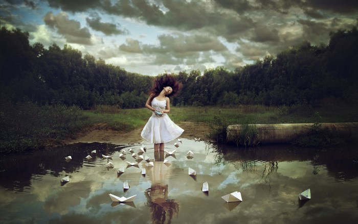 Woman in white dress with paper boats in water