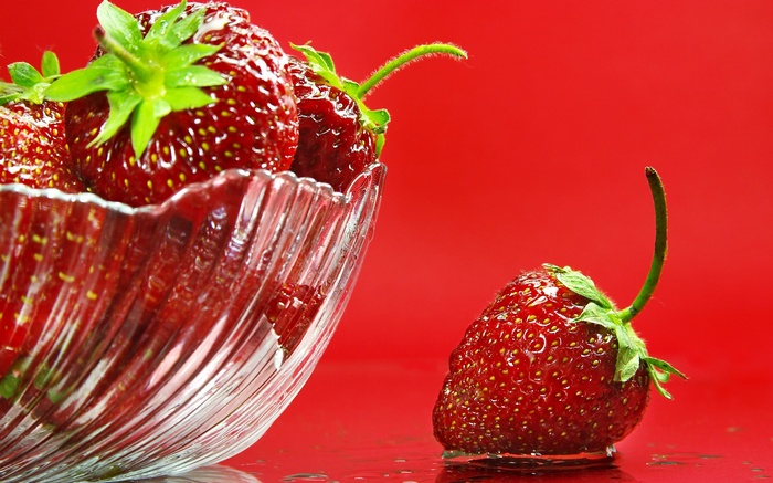 Strawberries in a glass bowl and on a red surface