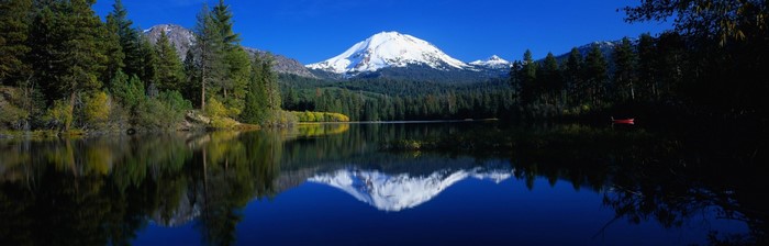 Snow-capped mountain reflected in a calm lake with pine trees