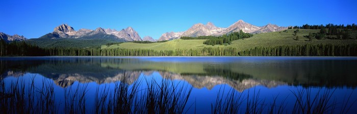 Mountain range reflected in a calm lake with tall grass