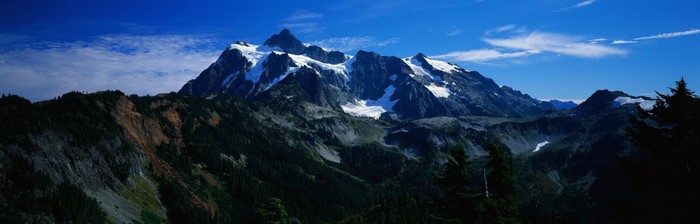 Snow-capped mountains and forested slopes under a blue sky
