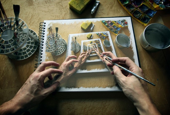 Artist's hands drawing a surreal perspective of art supplies