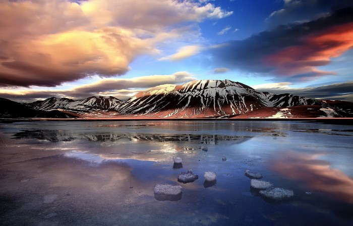 Snowy mountains reflected in a frozen lake at sunset