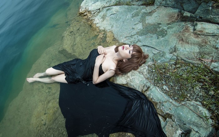 Woman in black dress lying on rocks by water