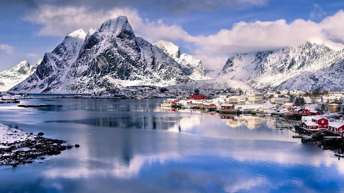 Snowy mountains and village reflected in a fjord in Norway