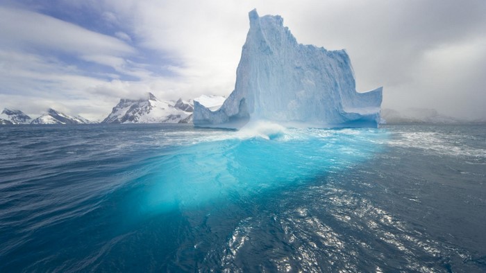 Iceberg in the ocean with snow-capped mountains