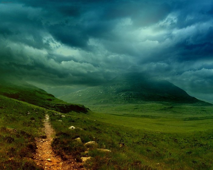 Mountain valley with a path under stormy clouds