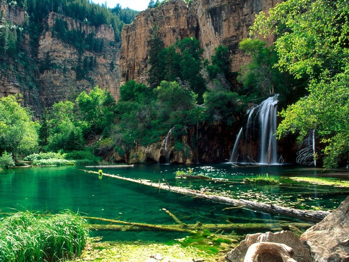 Waterfall cascading into a clear emerald lake surrounded by cliffs and trees