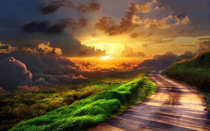 Road through a grassy hill at sunset with clouds