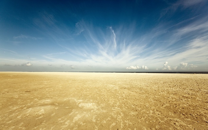 Vast sandy beach under a wide blue sky with wispy clouds