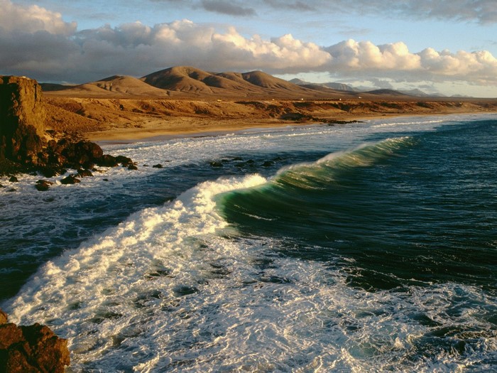 Ocean wave crashing on a rocky shore with mountains in the background