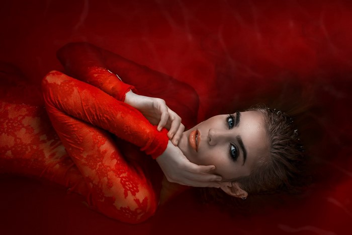 Woman in red lace dress submerged in red liquid