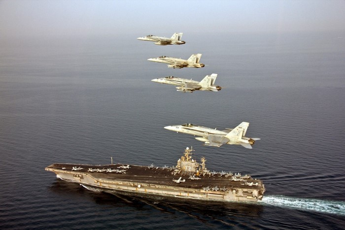 Aircraft carrier with F/A-18 Hornets flying in formation