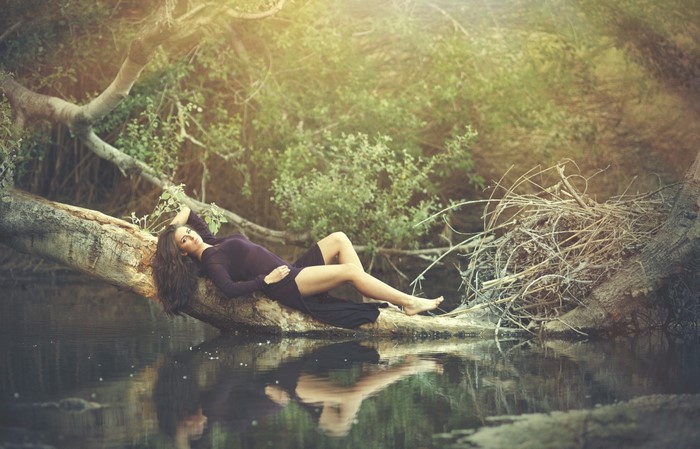 Woman lying on a fallen tree over water