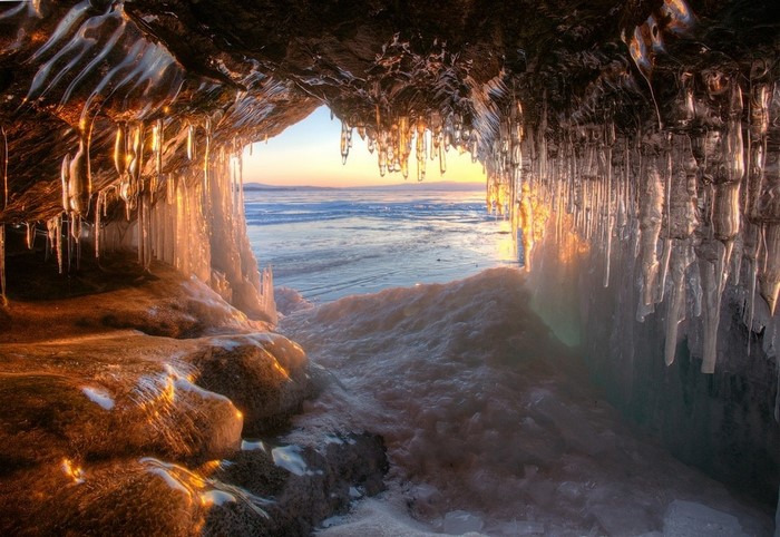 Ice cave with icicles overlooking a frozen lake at sunset