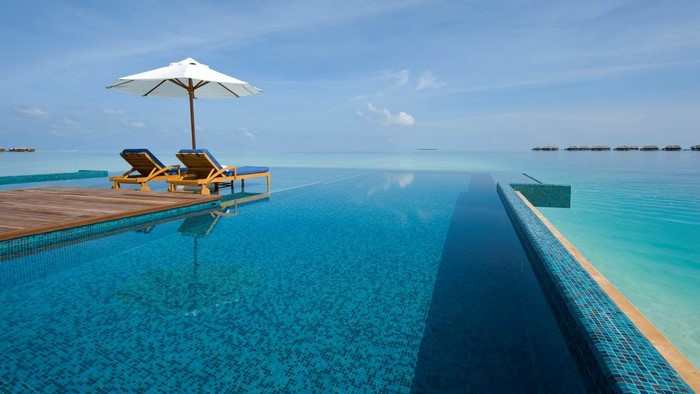 Infinity pool overlooking the ocean with lounge chairs and umbrella