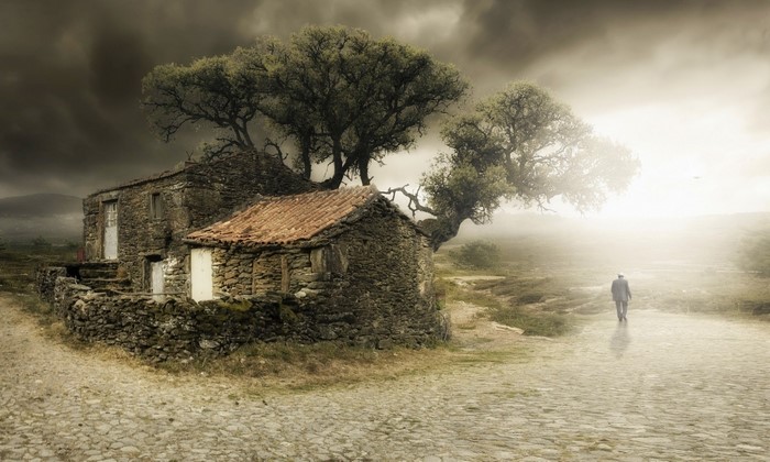 Man walks away from old stone houses in misty landscape