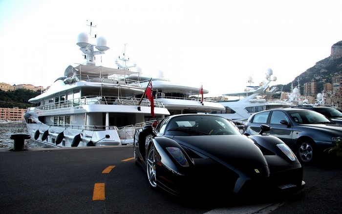 Black Ferrari parked by yachts in a harbor