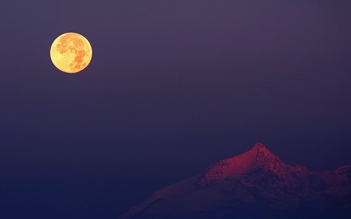 Full moon over illuminated mountain peak at dusk