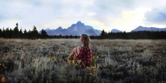 Woman sitting in a field with mountains in the background