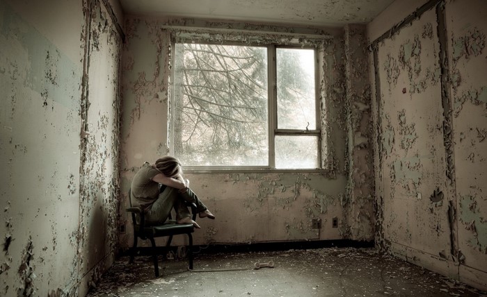 Woman sitting alone in a ruined room by a window
