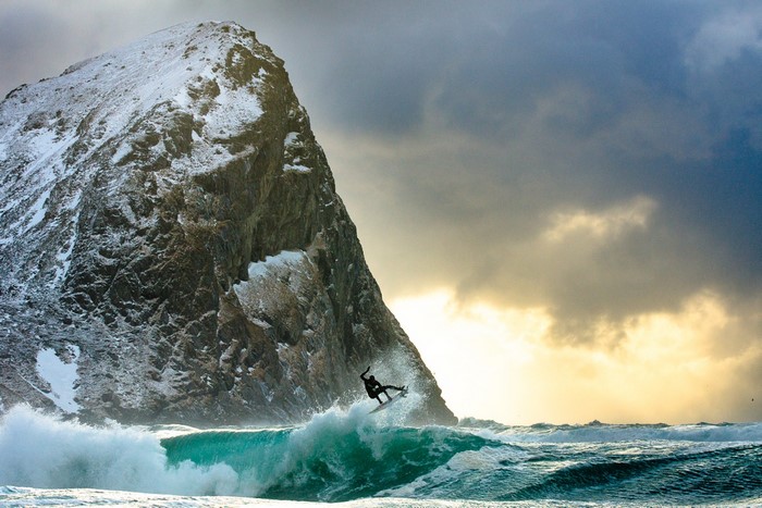 Surfer catches a wave near a snow-capped mountain