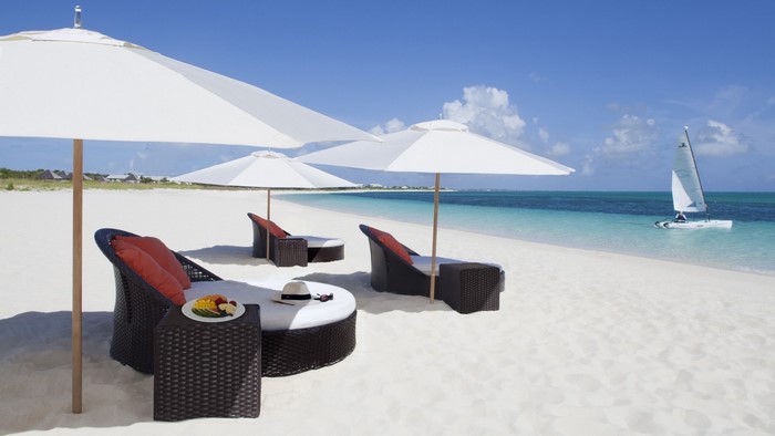 Tropical beach with lounge chairs, umbrellas, and sailboat