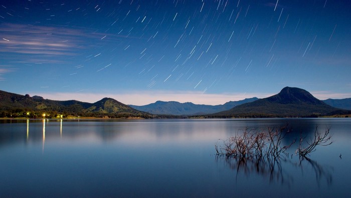 Star trails over a lake with mountains at night