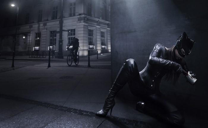 Catwoman in a dark alley with a cyclist in the background