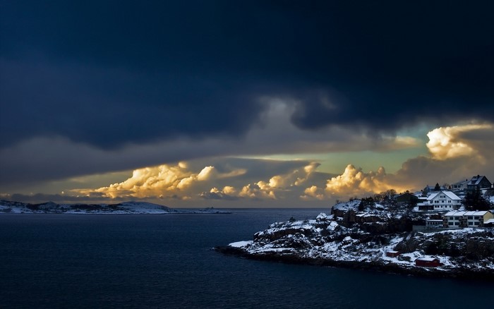 Snowy coastal village under dramatic clouds at sunset