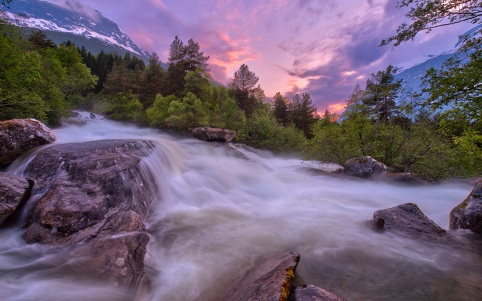 River flowing through a forest with mountains at sunset