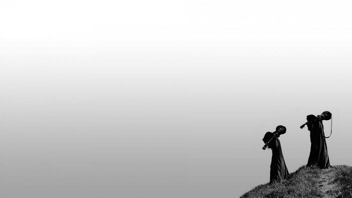 Two figures in silhouette carrying guitars on a grassy hill