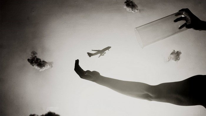 Monochrome photography of hands holding airplane with clouds