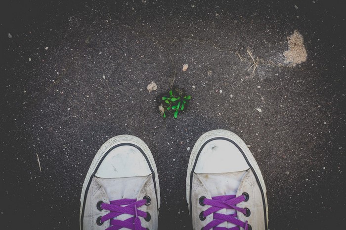 Pair of white sneakers with purple laces on asphalt