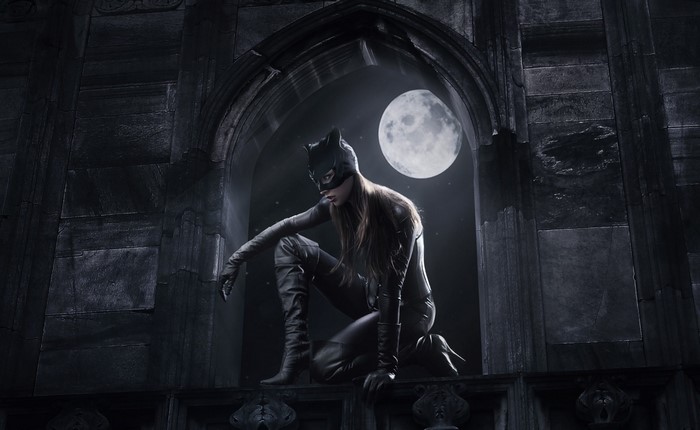 Catwoman in a black suit crouching on a ledge at night