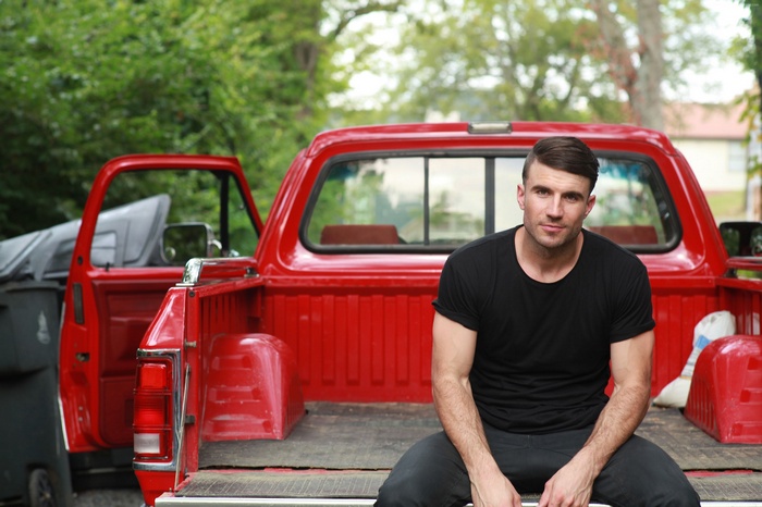 Sam Hunt sitting in the back of a red pickup truck