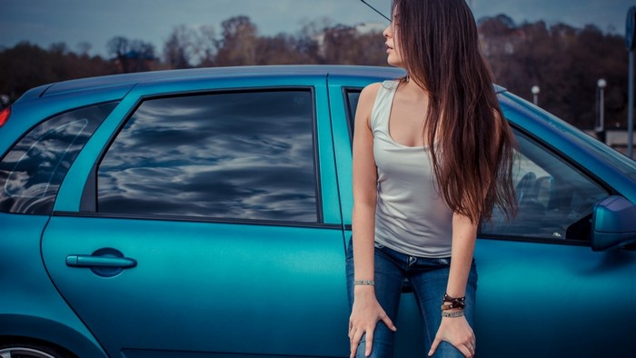 Woman in jeans leaning on a blue car