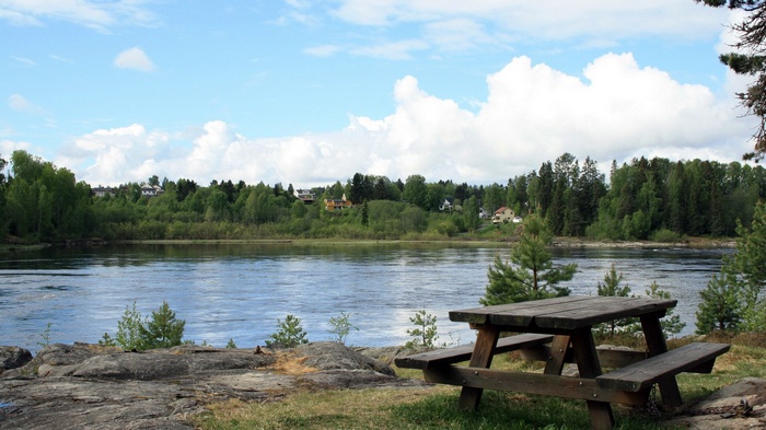 Wooden picnic table by a river with trees and houses
