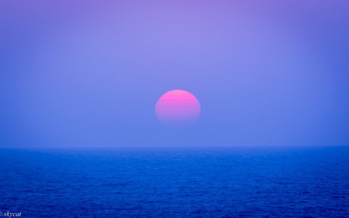 Pink sun setting over the ocean horizon