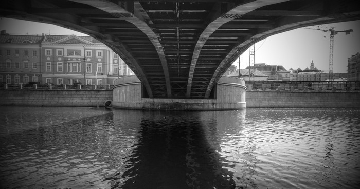 Under a bridge over a river with buildings and a crane in the background