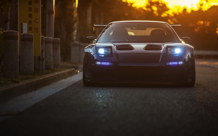 Dark Honda NSX sports car with headlights on at sunset