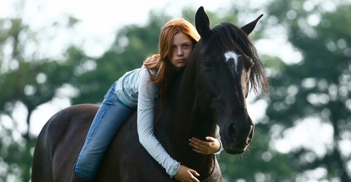 Young woman with red hair hugging a dark horse