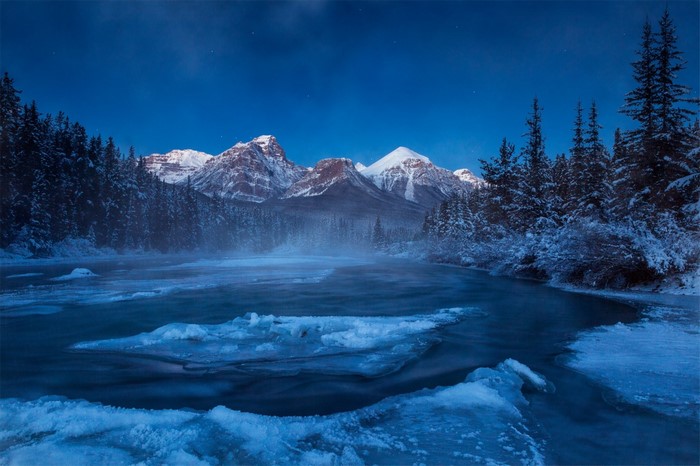 Winter night landscape with mountains, river, and snow-covered trees