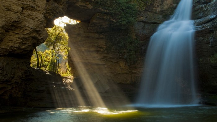 Waterfall cascading through rock formation with sun rays