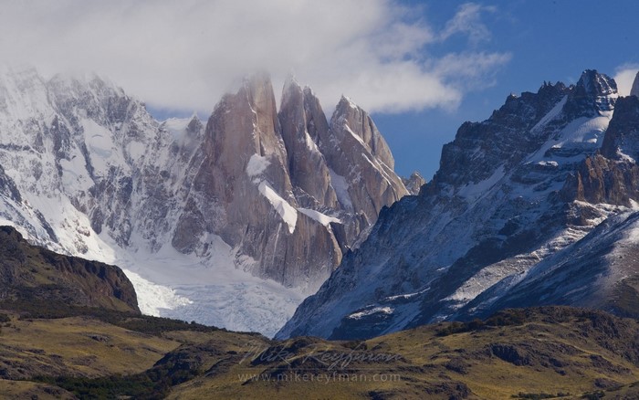 Jagged snow-capped mountains under a cloudy blue sky