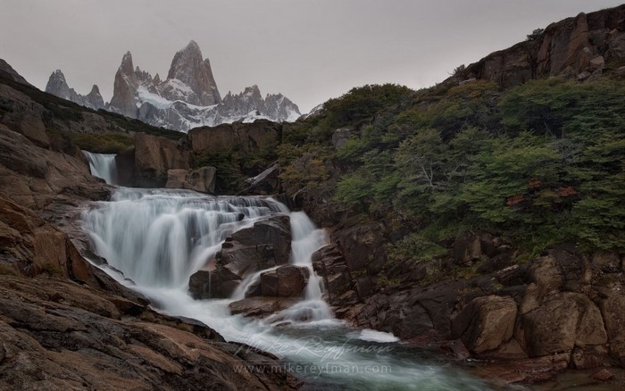 Waterfall cascading down rocks with mountains in the background